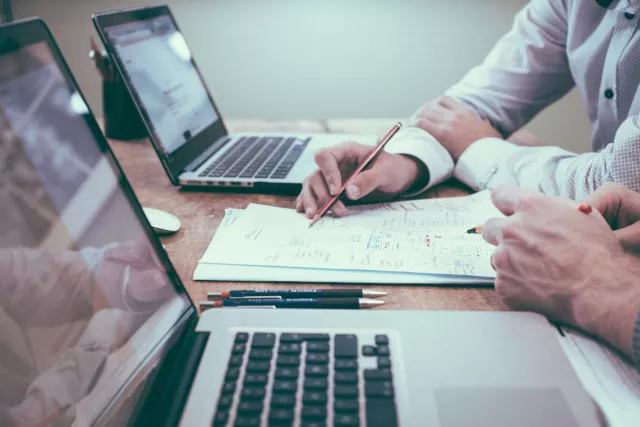 stock image showing co-workers with laptops and workings on a piece of paper