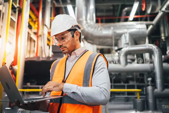 Professional worker of modern factory using laptop controlling program to automatic machinery.