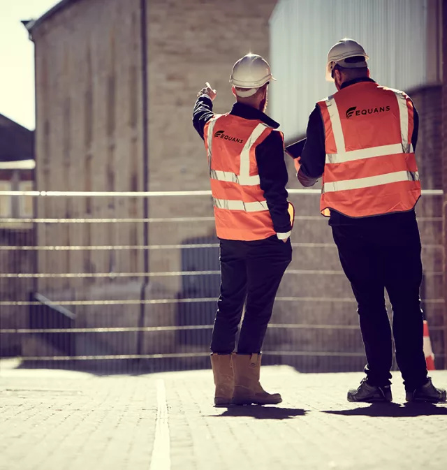 Equans employees from behind stood on a regeneration site in High vis vests and hard hats