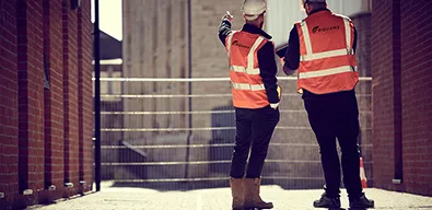 Equans employees from behind stood on a regeneration site in High vis vests and hard hats