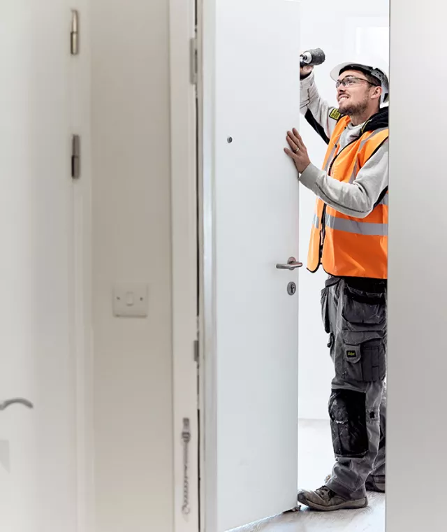 An equans employee fixing a hanging door