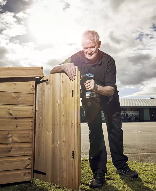 An Equans handyman fixing a wooden bin store