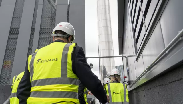 An Equans employee from behind wearing a high vis vest and hard hat